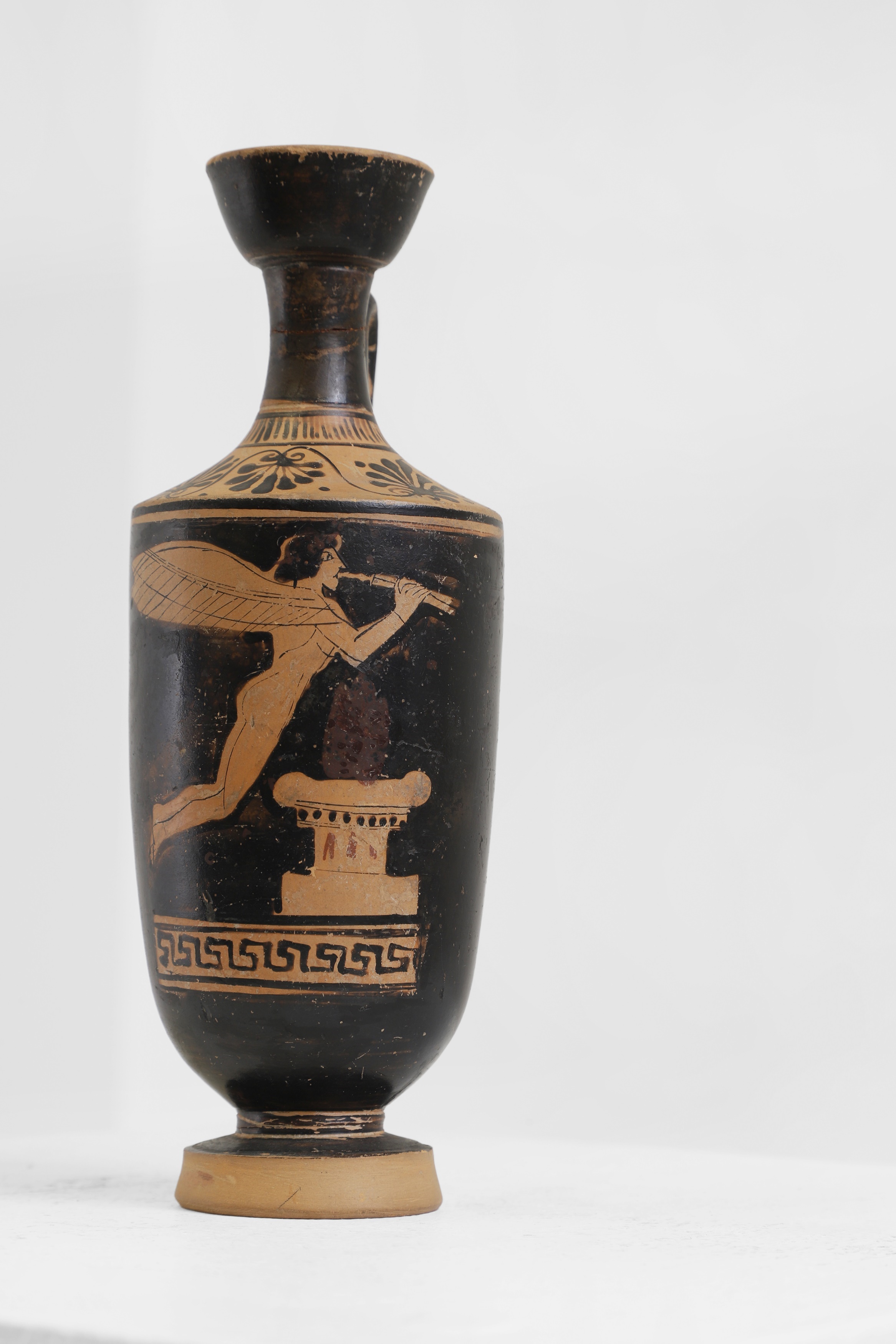 An Attic red-figure lekythos, c.5th century BC, Greek, attributed to the Bowdoin Painter (c.475-425 BC), decorated with Eros playing pipes over a funerary altar, with linked palmettes to the shoulder, 6.5cm wide 19cm high